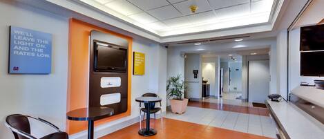 A lobby with a reception desk, a seating area with chairs, a potted plant, and a sign on the wall.