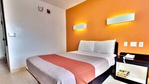 A hotel room with a bed, a nightstand with a phone and a book, and a wall-mounted light fixture.