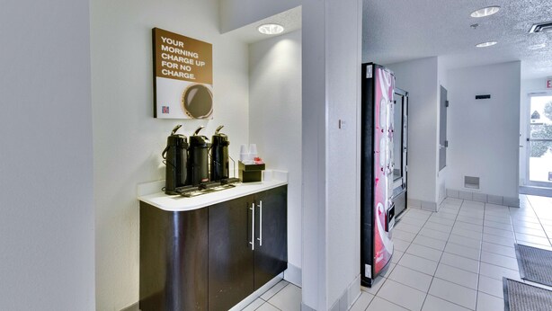 A modern kitchen with a coffee station, a large refrigerator, and a wall-mounted mirror.