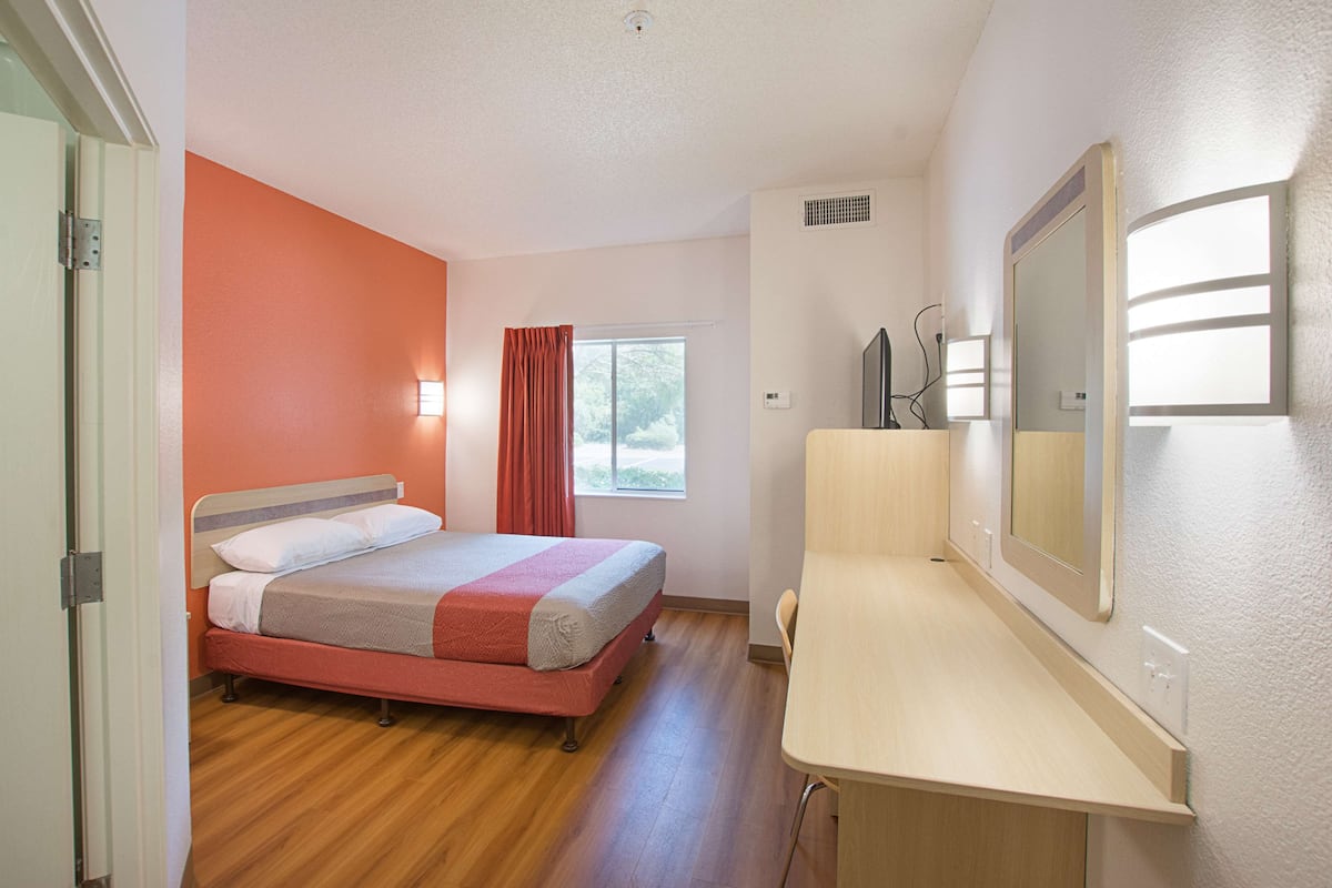 A hotel room with a bed, a desk, and a window.