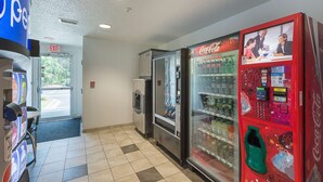 A vending area with Coca-Cola machines and a refrigerator, a door leading outside, and a blue sign with "OPEN" on it. - Motel 6 Columbia, SC - Fort Jackson Area (Columbia)