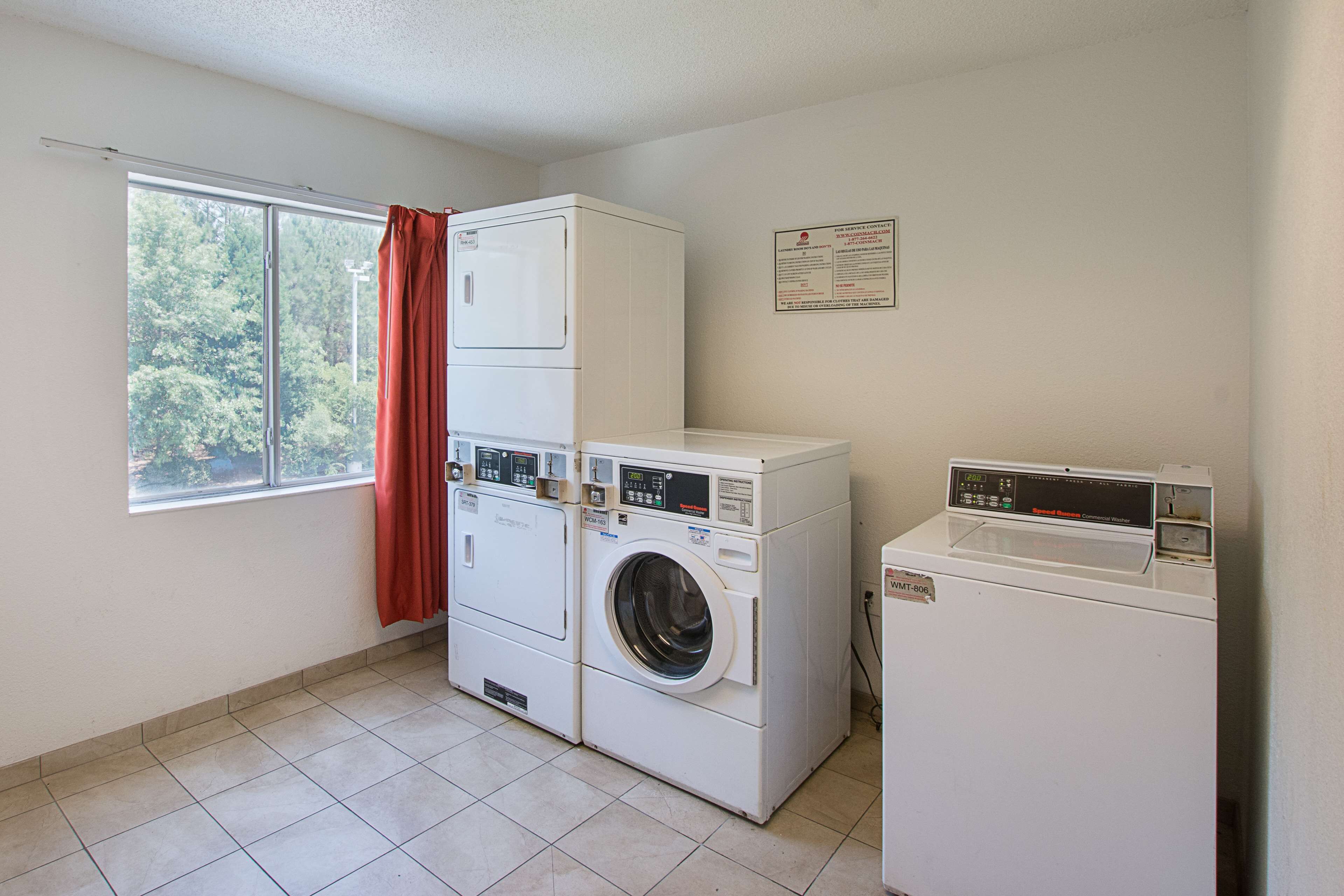 A laundry room with stacked washers and dryers, a window with a view of trees, and a notice on the wall.