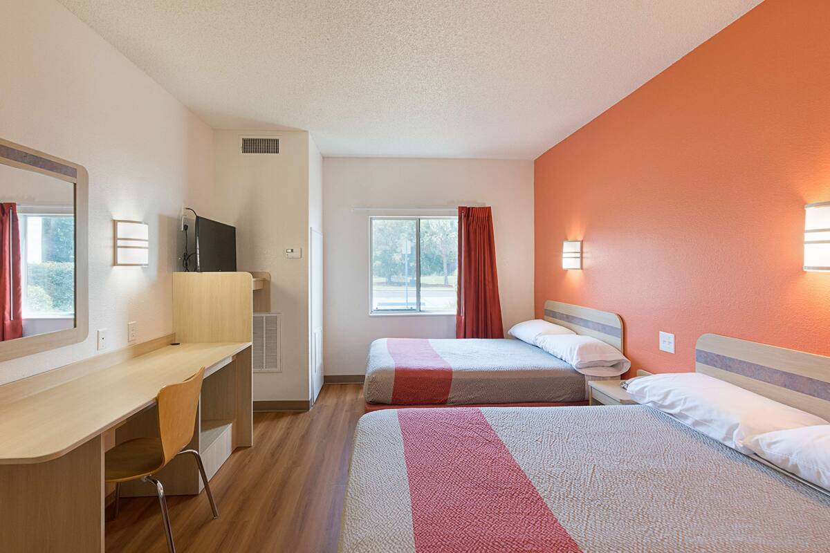 A hotel room with two beds, a desk, a TV, and a window with curtains.