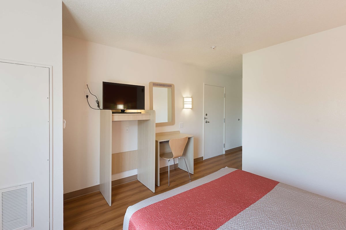 A hotel room with a bed, a desk, a chair, a television, and a wardrobe.