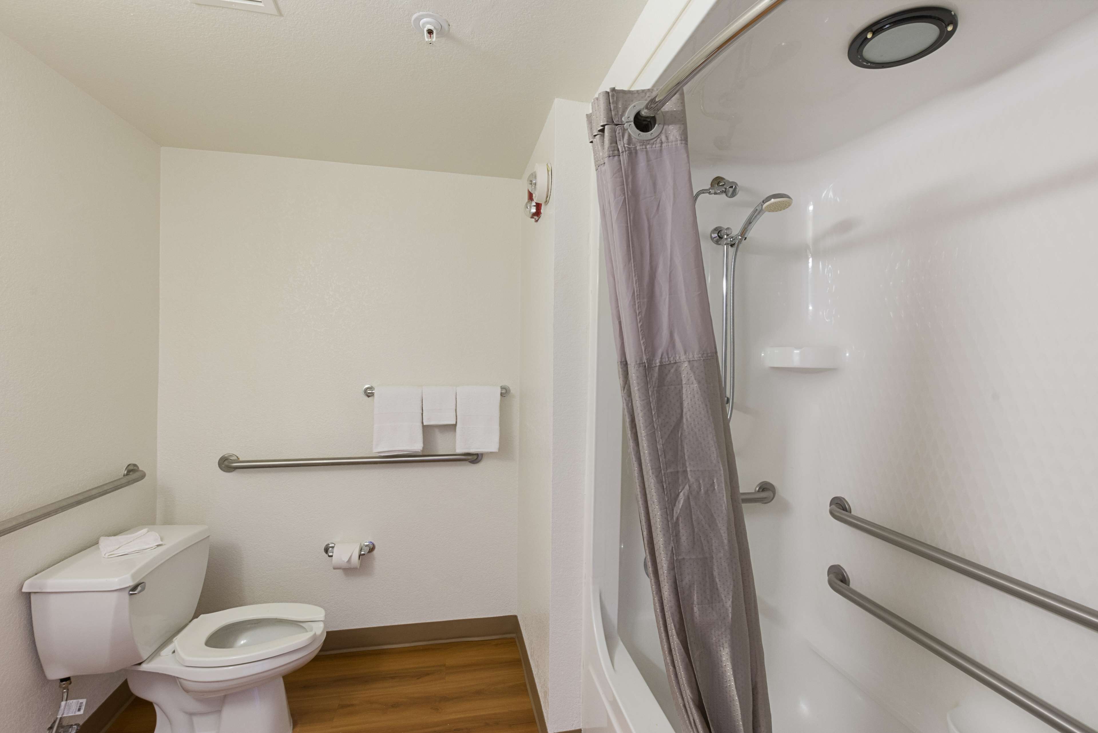 Et badeværelse med toilet, brusebad med glasdør og gelænder.
