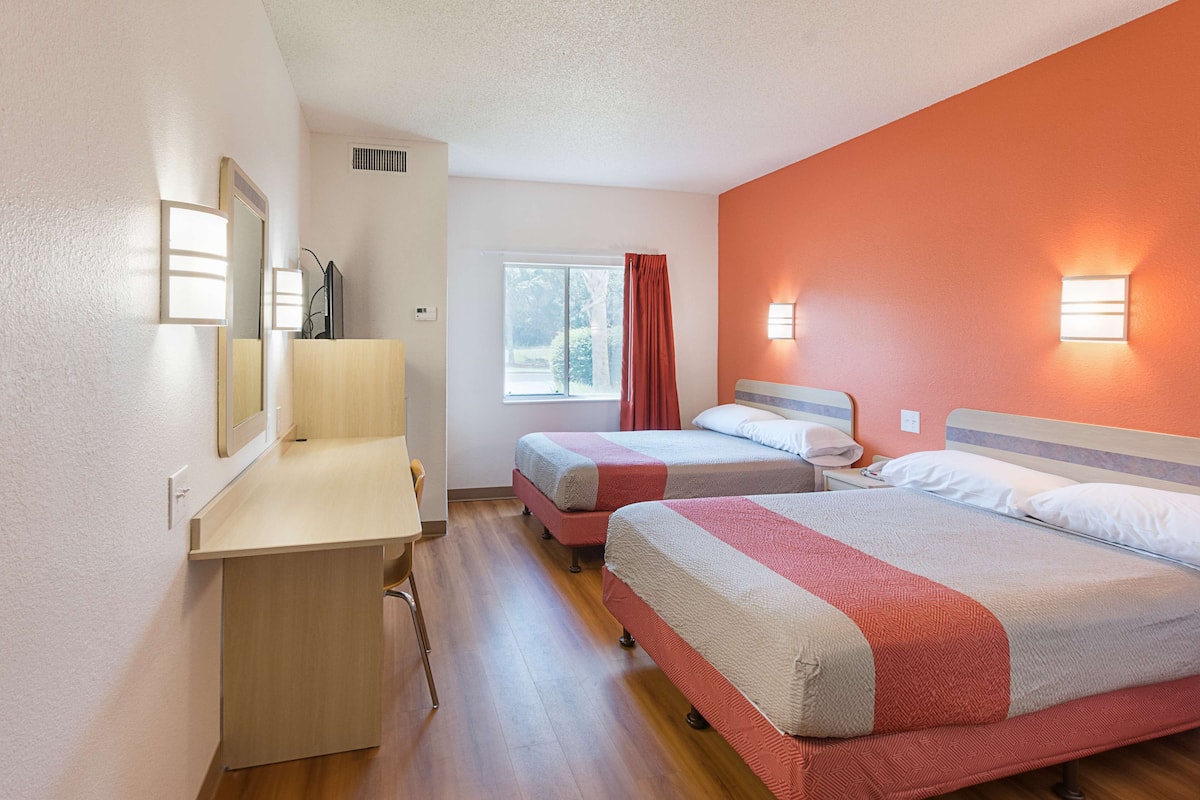 A hotel room with two beds, a desk, a window with a view, and a mirror.