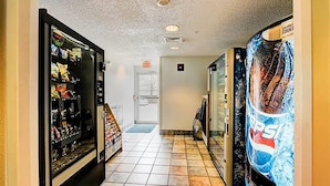 A corridor with vending machines on both sides, a tiled floor, and an exit door at the end.