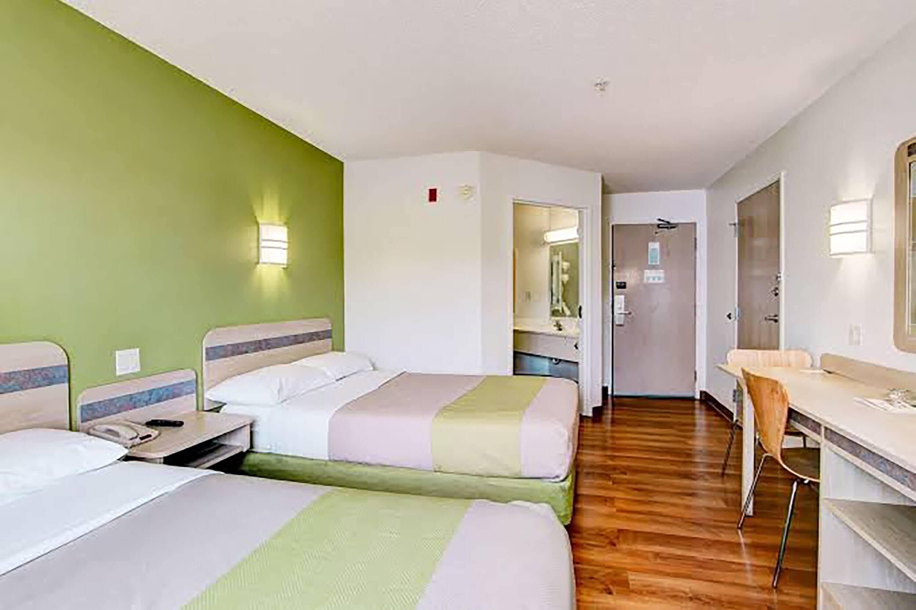A hotel room with two beds, a desk, and a mirror.