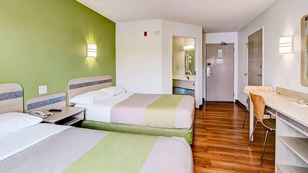 A hotel room with two beds, a desk, and a chair. There is a mirror on the wall and a door leading to a bathroom.