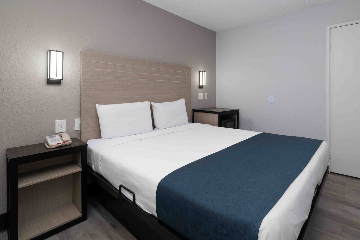 A hotel room with a bed, bedside tables, a phone, and wall-mounted lights.