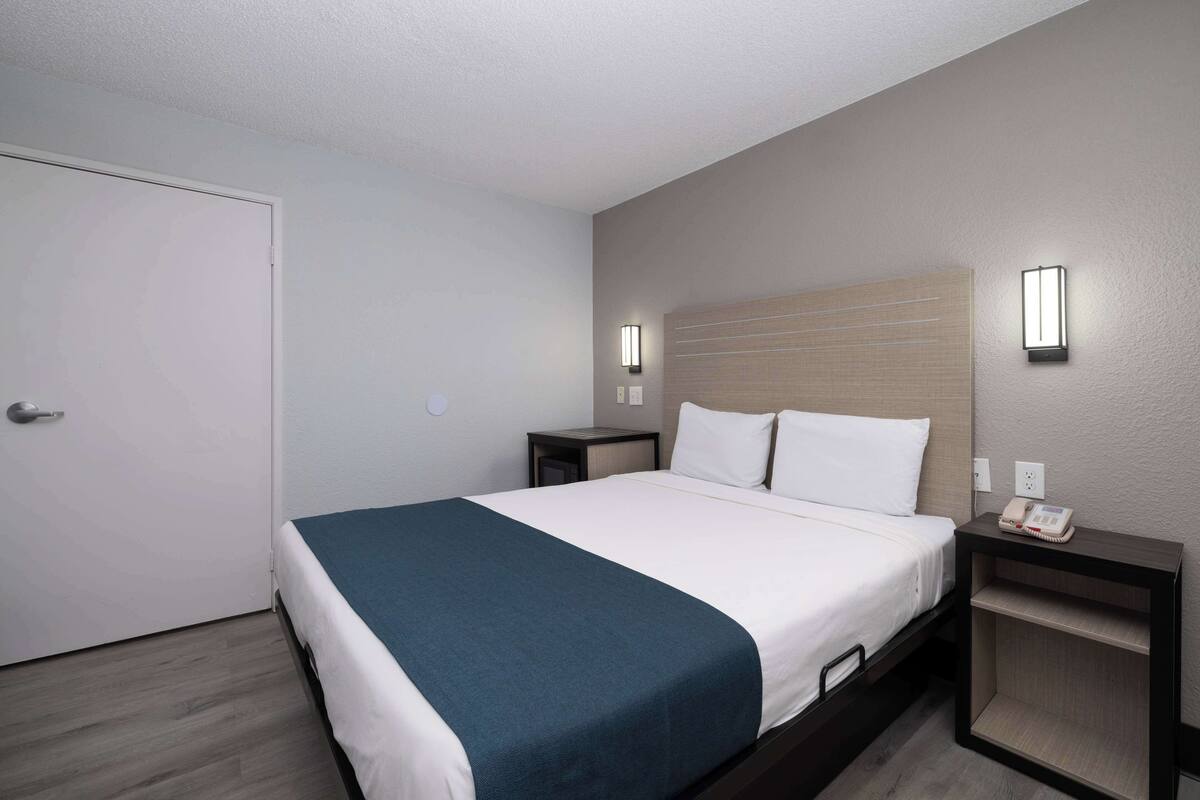 A hotel room with a bed, bedside tables, a telephone, and wall-mounted lights.