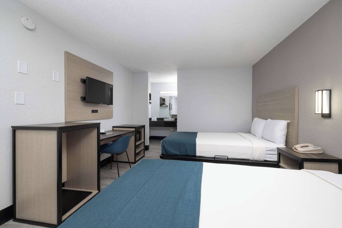 A hotel room with a desk, two beds, a TV, a phone, and a mirror.