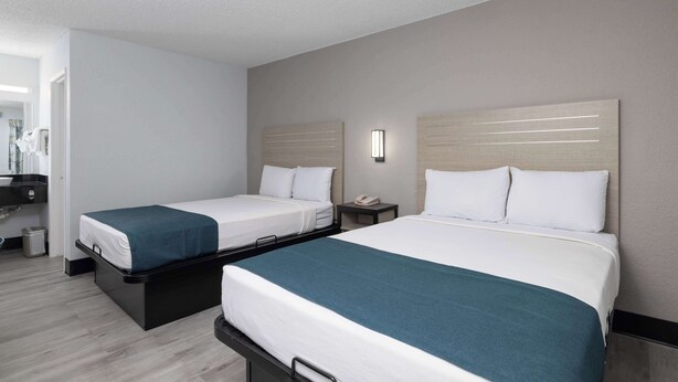 A hotel room with two beds, a bedside table with a phone, and a small trash bin. - Motel 6 Tempe, AZ - Broadway - ASU (Tempe)