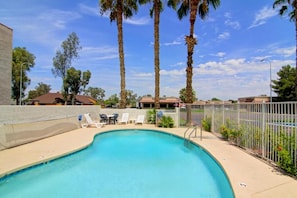 A swimming pool with lounge chairs and a fence.