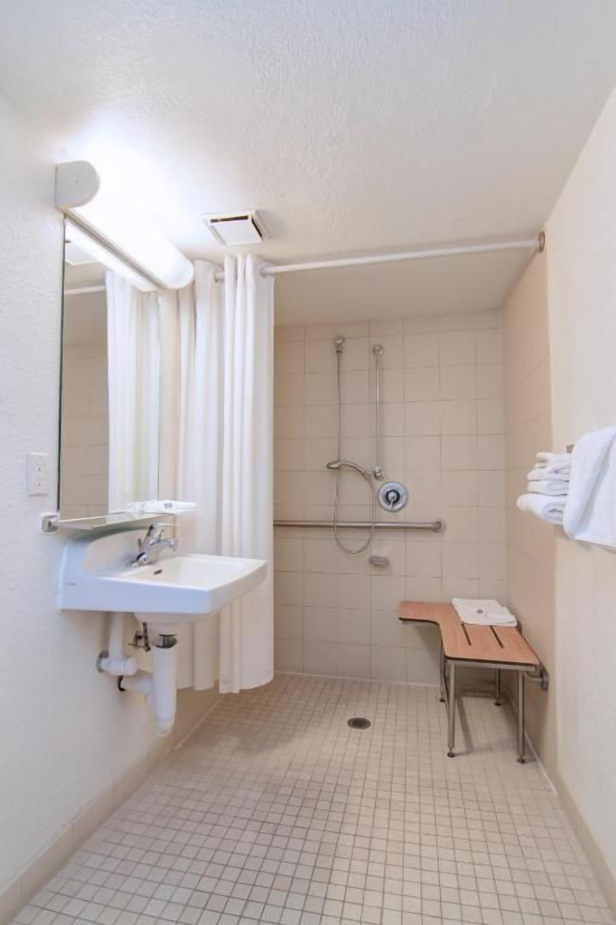 A small bathroom with a sink, mirror, shower, and a towel rack.