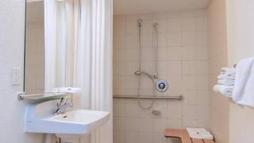A small bathroom with a sink, mirror, shower, and a towel rack.