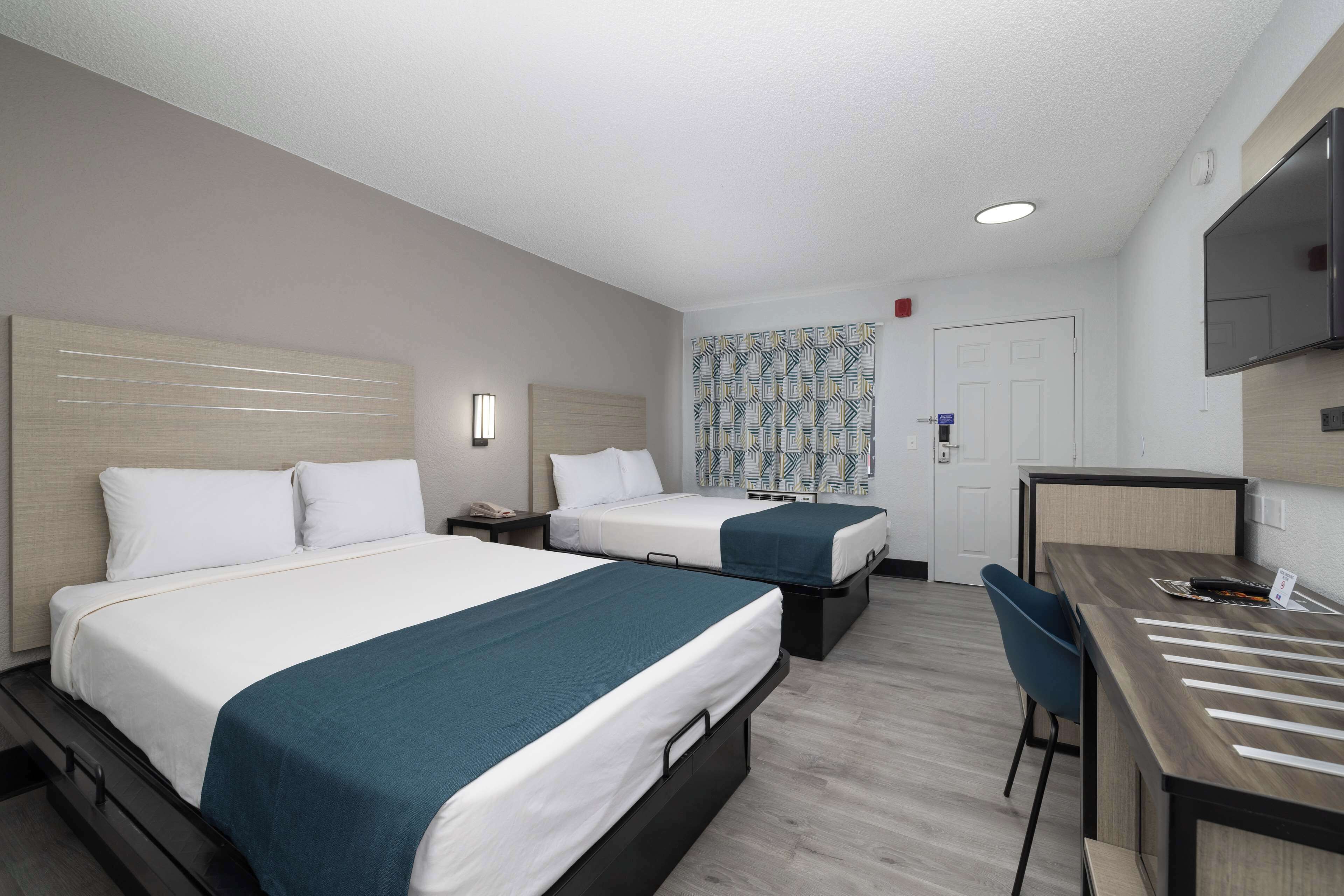 A hotel room with two beds, a desk, a chair, a TV, and a patterned curtain.