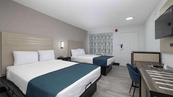 A hotel room with two beds, a desk, a chair, a TV, and a patterned curtain.
