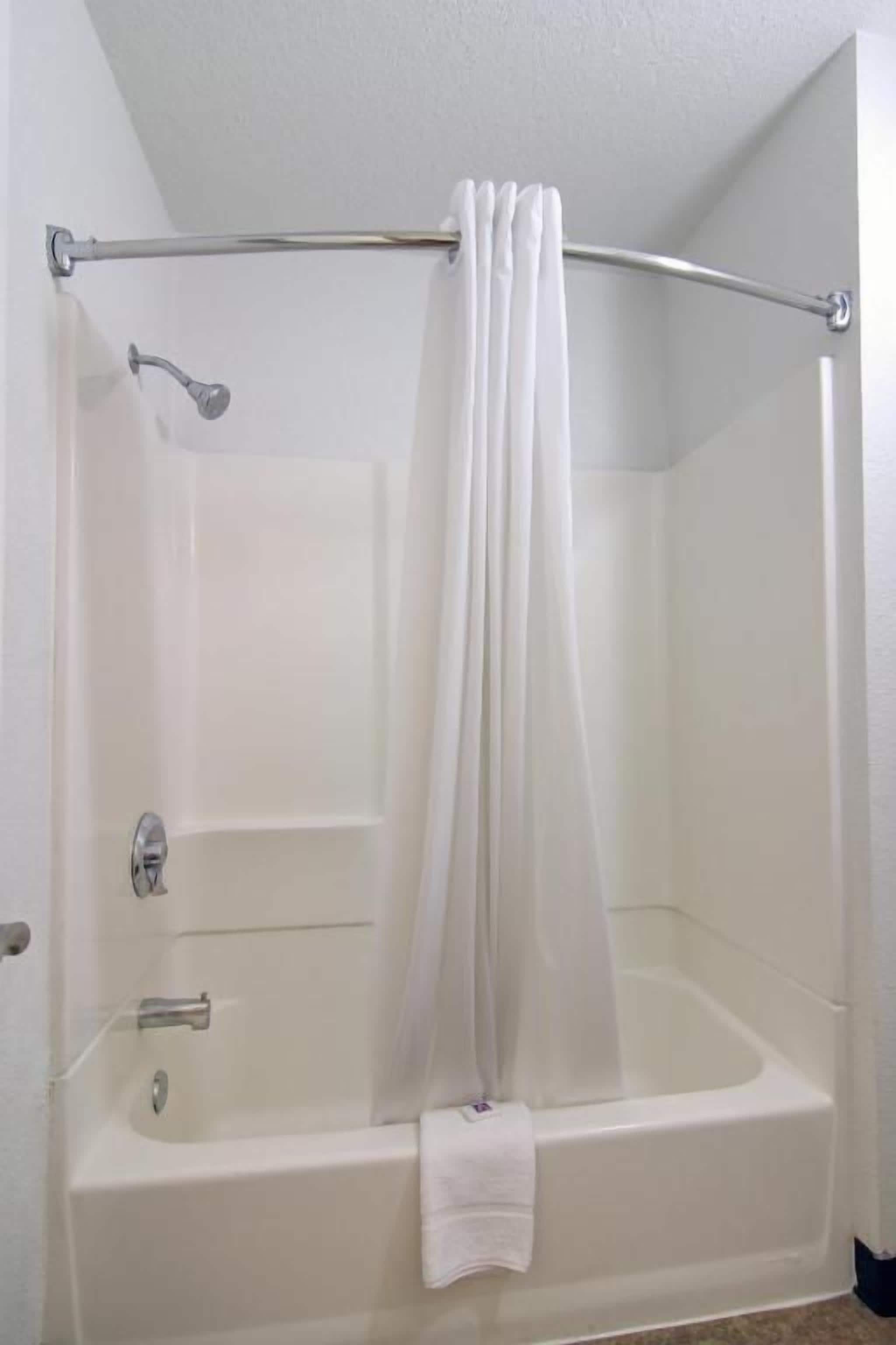 A white bathtub with a shower curtain rod and a towel.