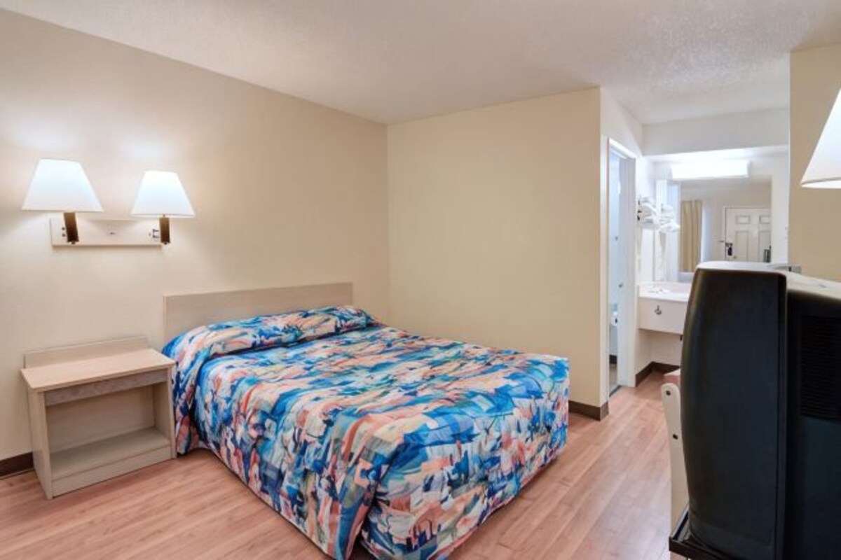 A hotel room with a bed, bedside table, lamp, and a television.