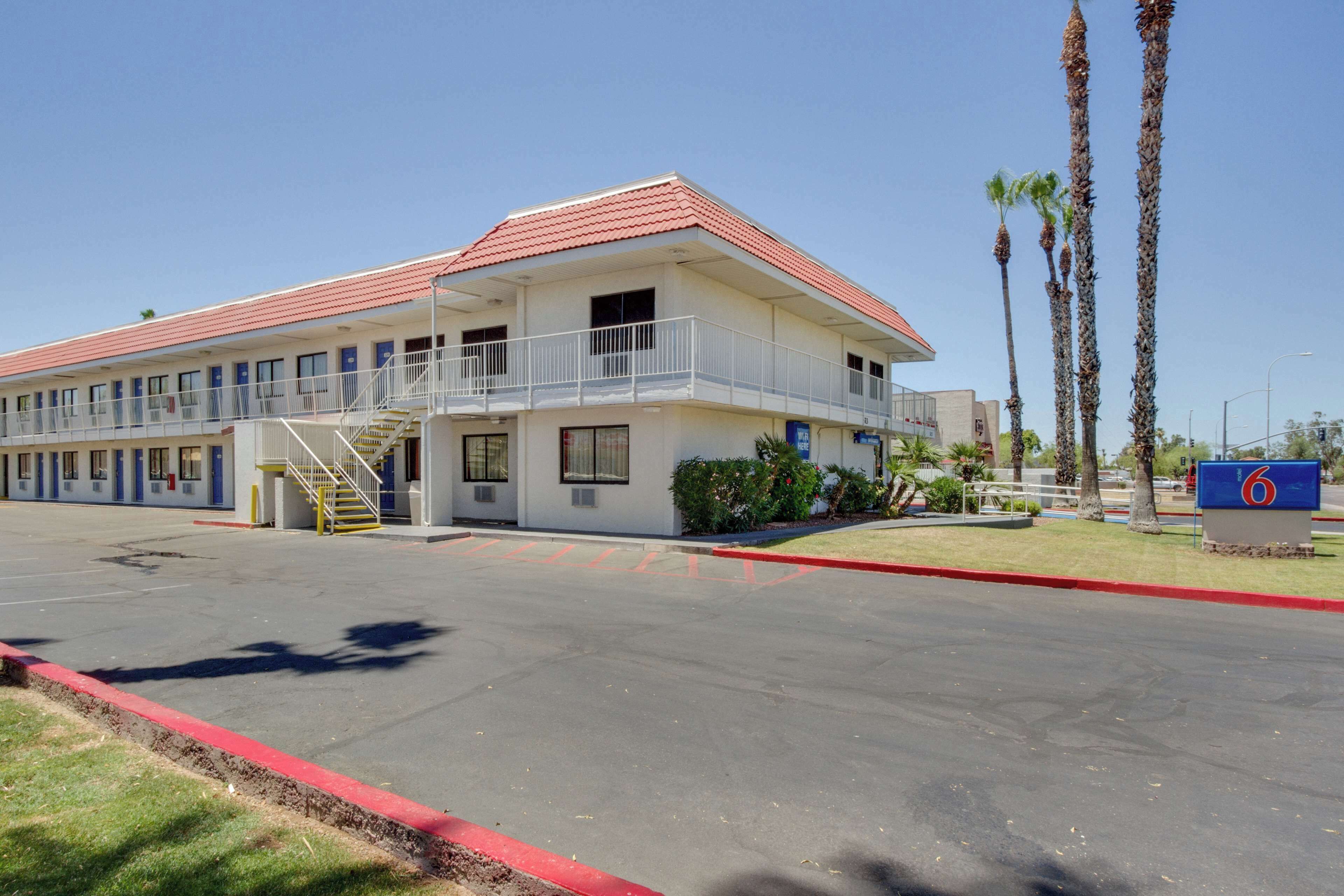 A motel with a red roof, multiple balconies, and a parking lot.