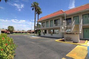 A motel with a red-tiled roof, a parking lot, and a palm tree.