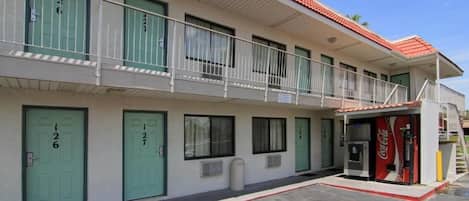 A two-story motel with numbered doors, a Coca-Cola vending machine, and a small outdoor area.