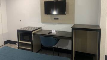 Habitación de hotel pequeña con una cama individual, un escritorio con silla, un televisor montado en la pared y un estante.