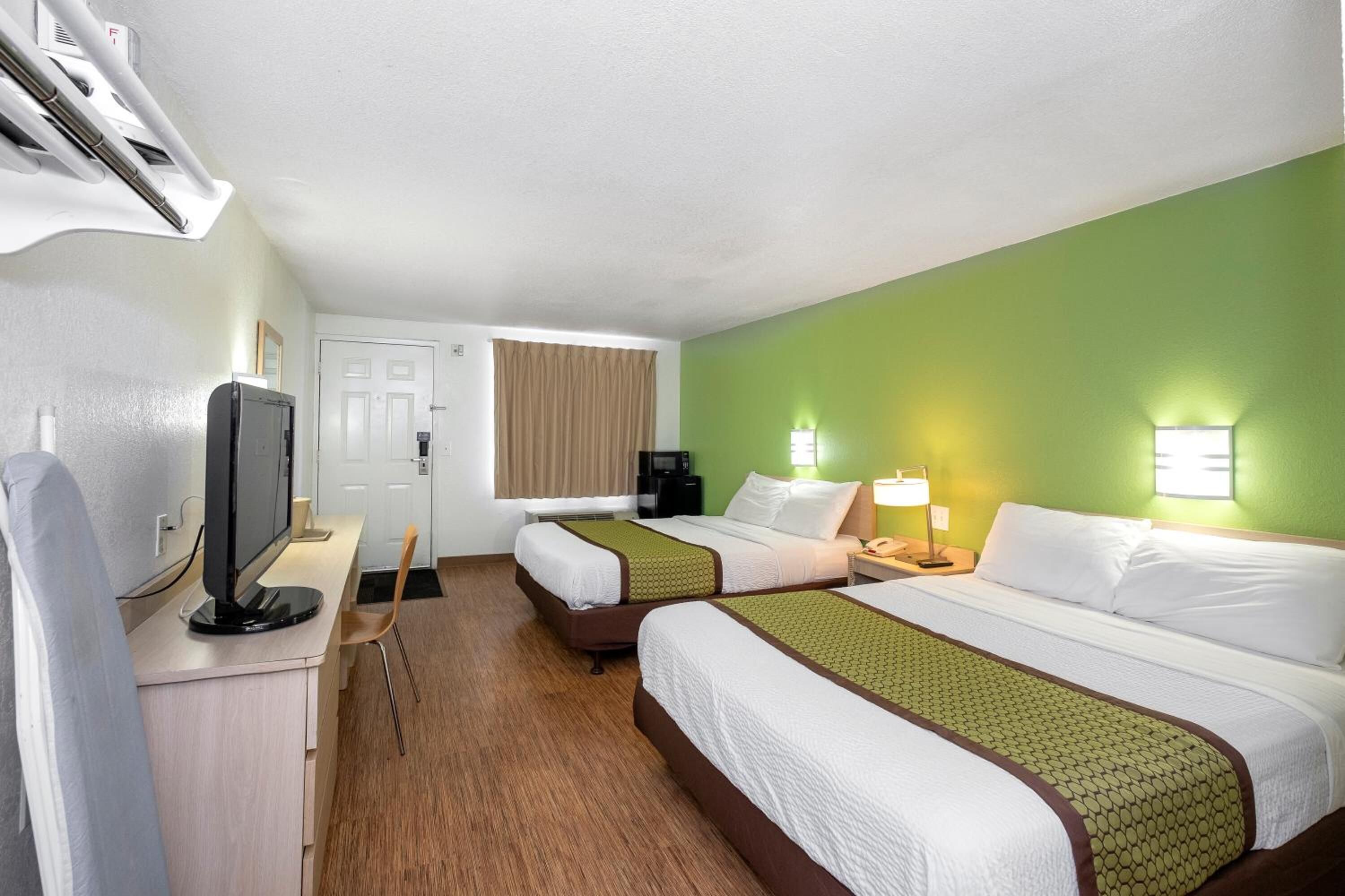 Una habitación de hotel con dos camas, un escritorio con computadora, televisor y cafetera.