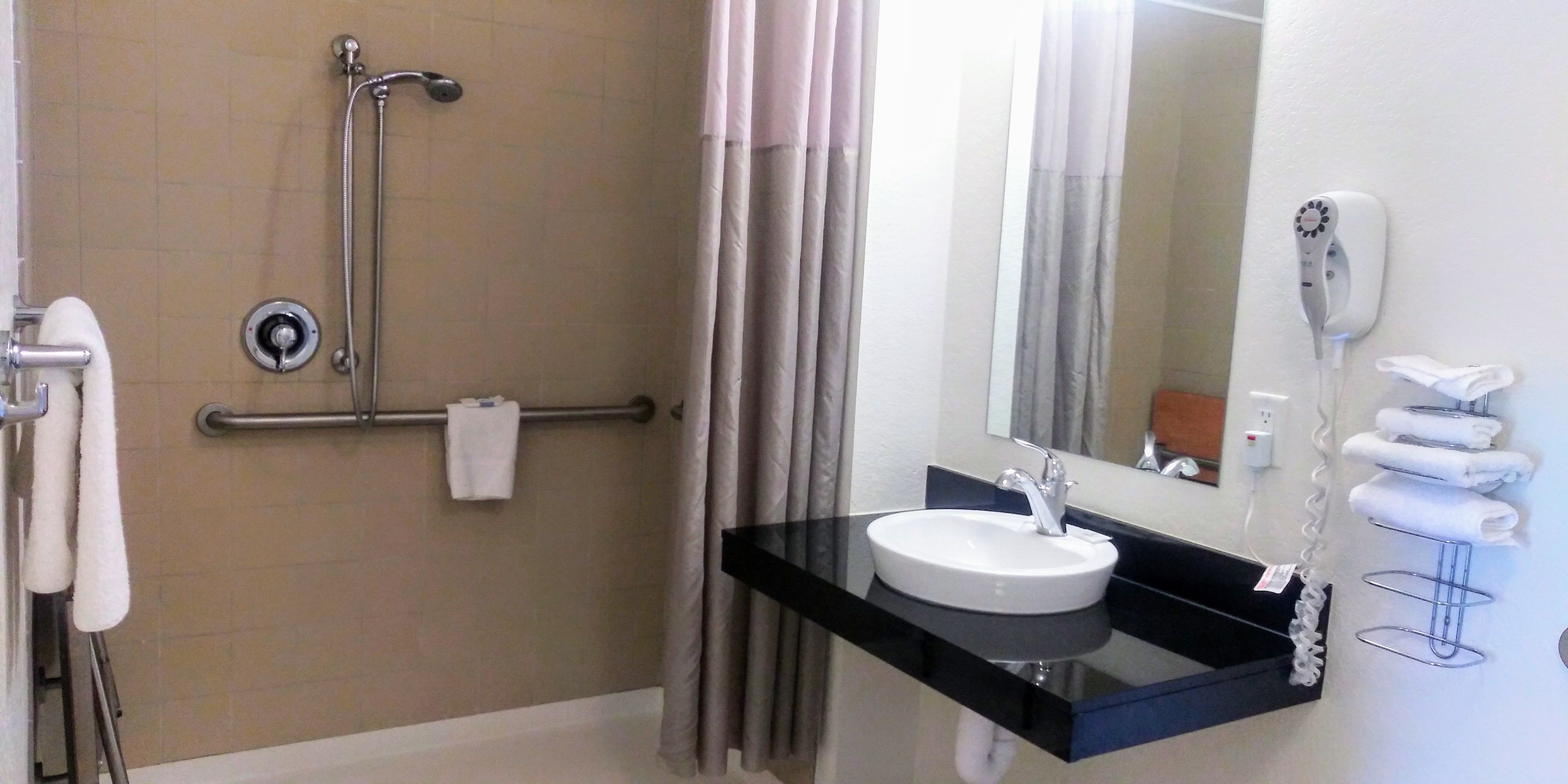 Een badkamer met een douche, een wastafel, een handdoekhouder en een haardroger.