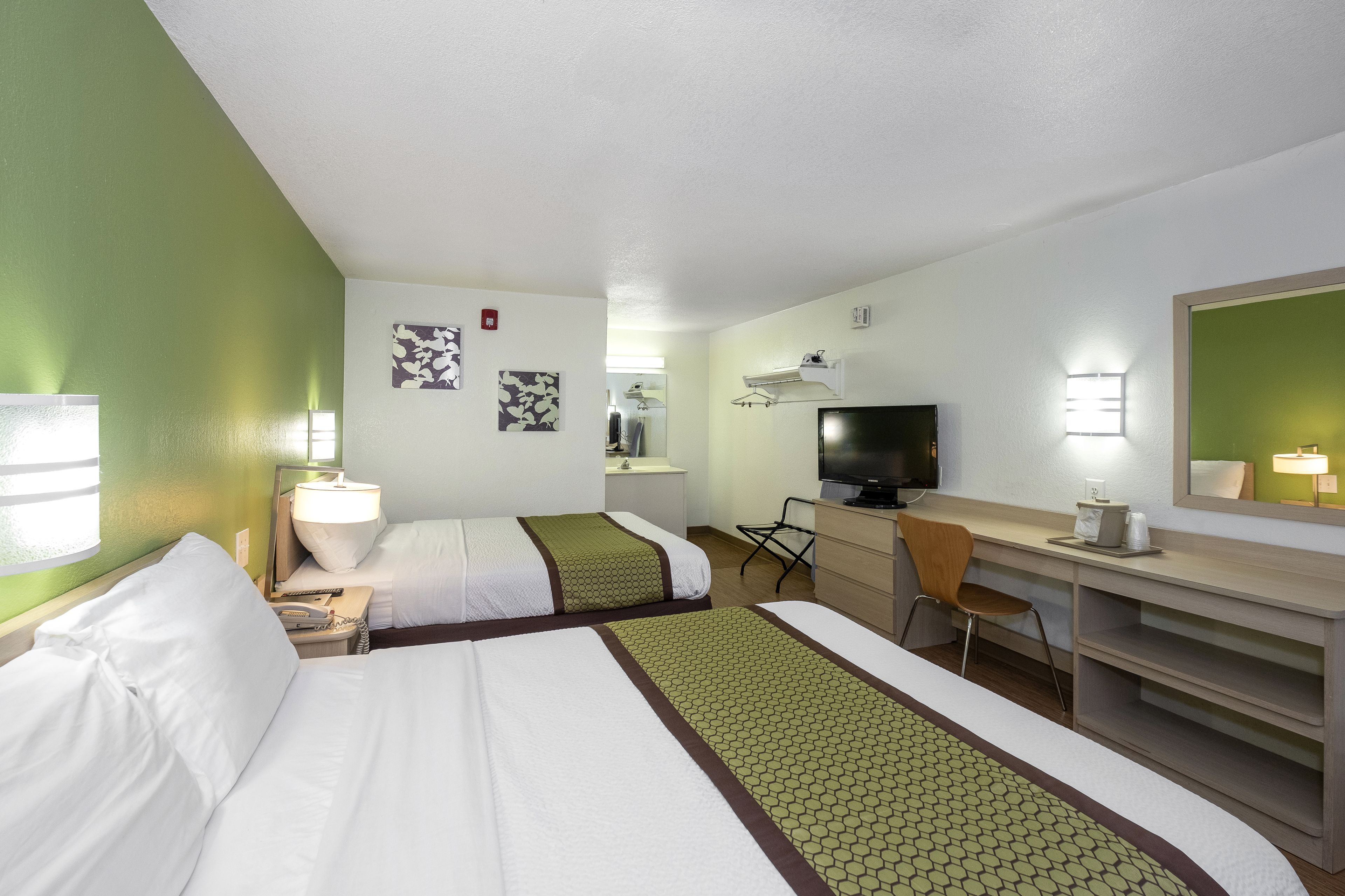 A hotel room with two beds, a desk, a chair, a television, and a mirror.