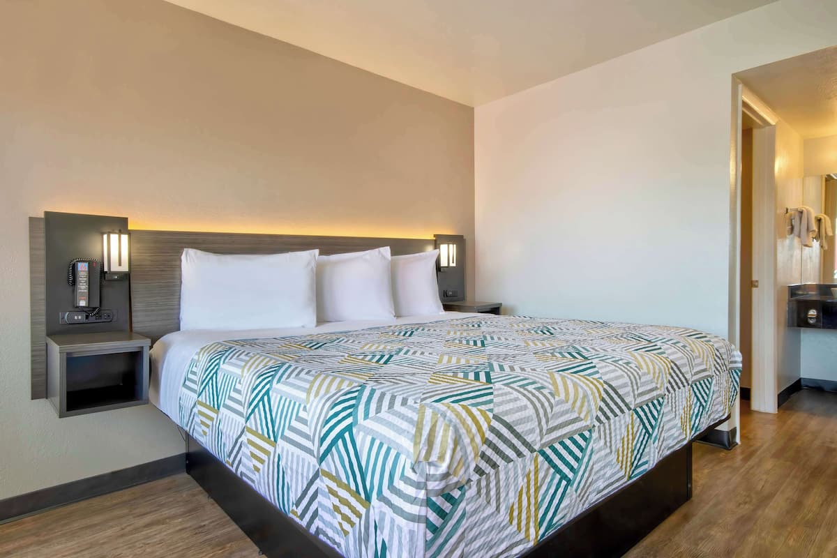 Una habitación de hotel con una cama grande, dos mesitas de noche, un buró, un teléfono montado en la pared y un escritorio pequeño con una lámpara.