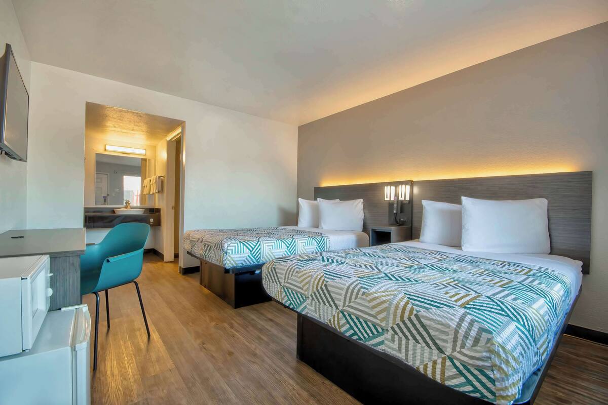 Habitación de hotel con dos camas, un escritorio, una silla y una kitchenette.