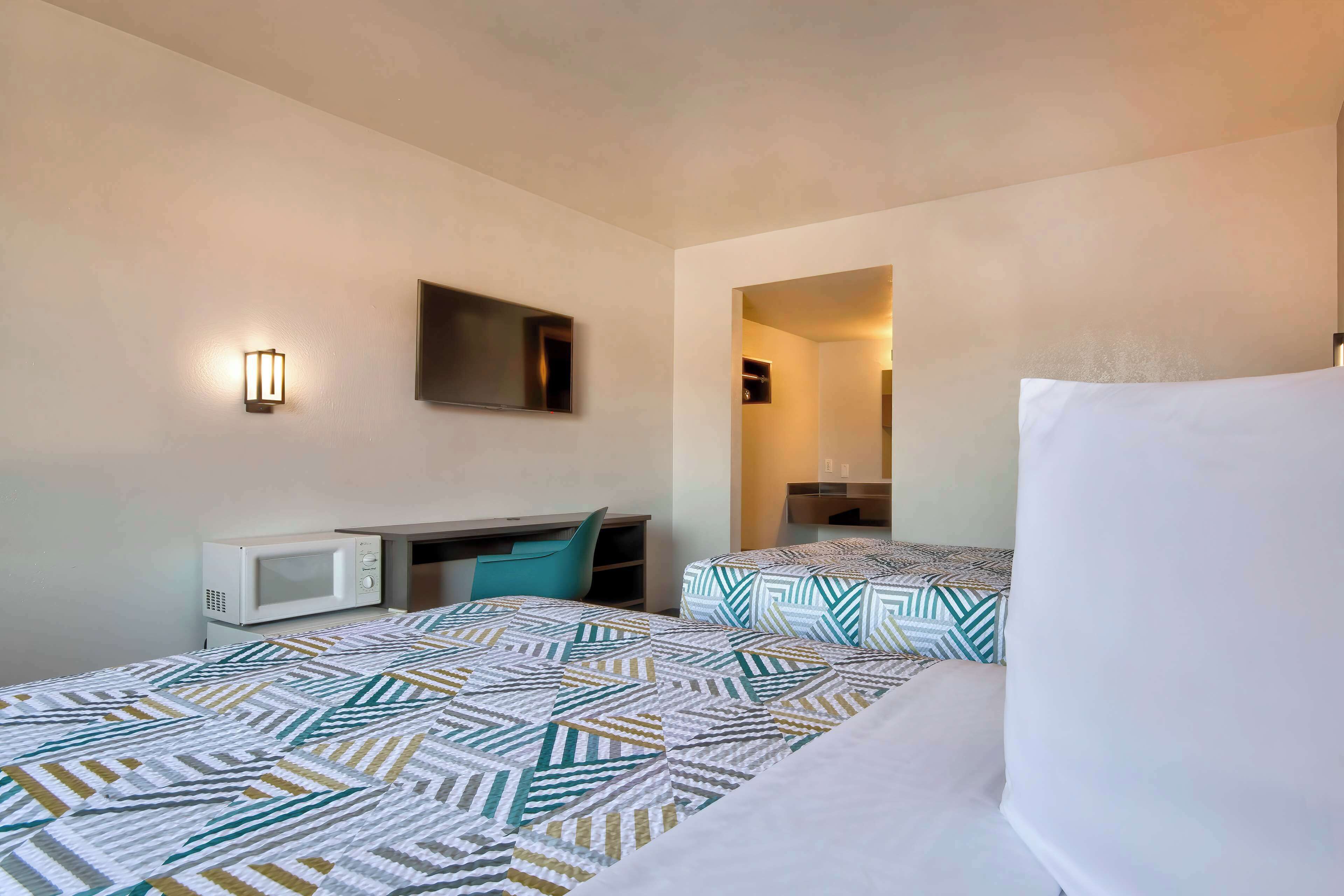 A hotel room with two beds, a microwave, a desk, and a TV.