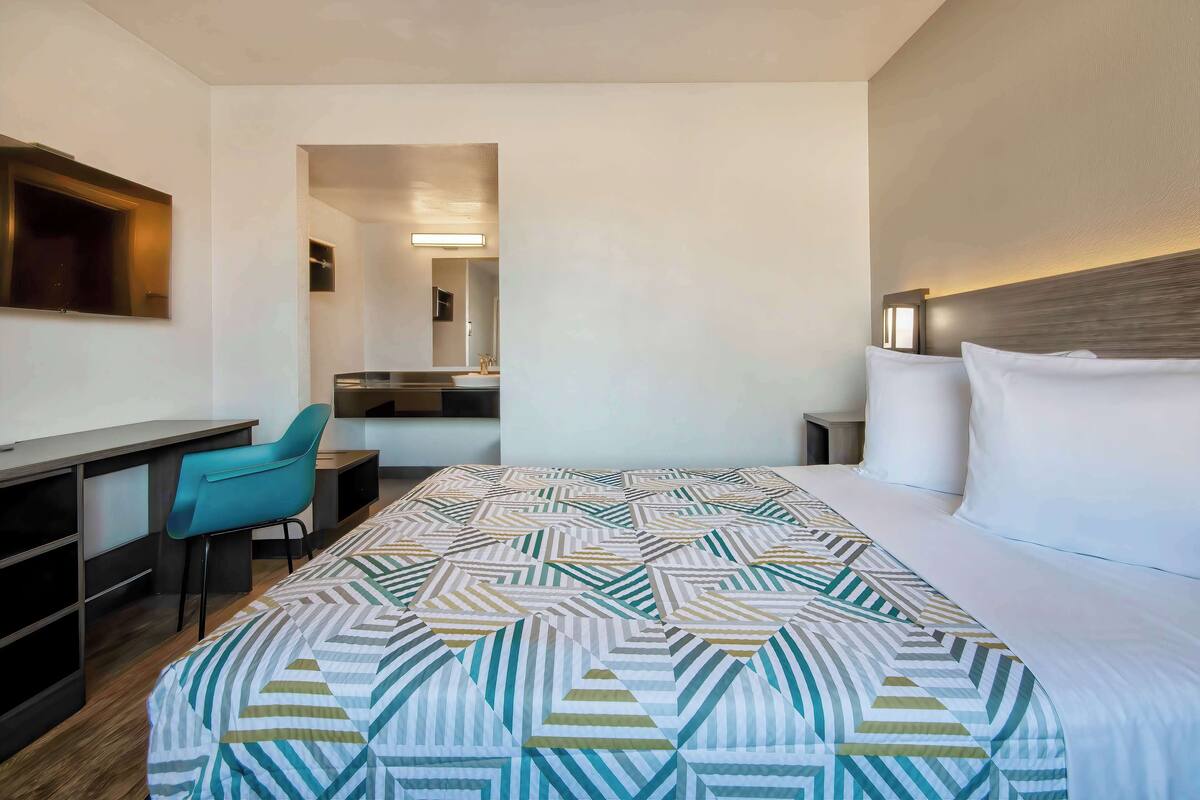 Habitación de hotel con cama, escritorio, silla y baño visible a través de una puerta abierta.