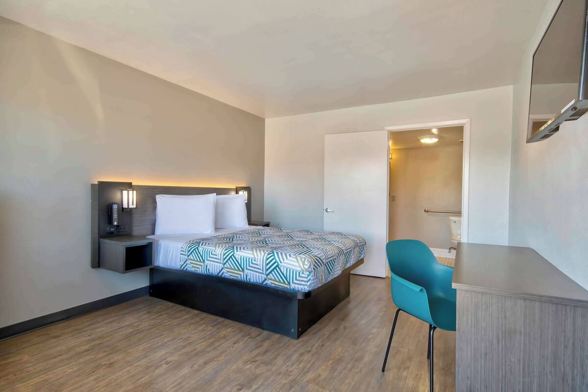 Una habitación de hotel moderna con cama, mesita de noche, silla y un pequeño escritorio.