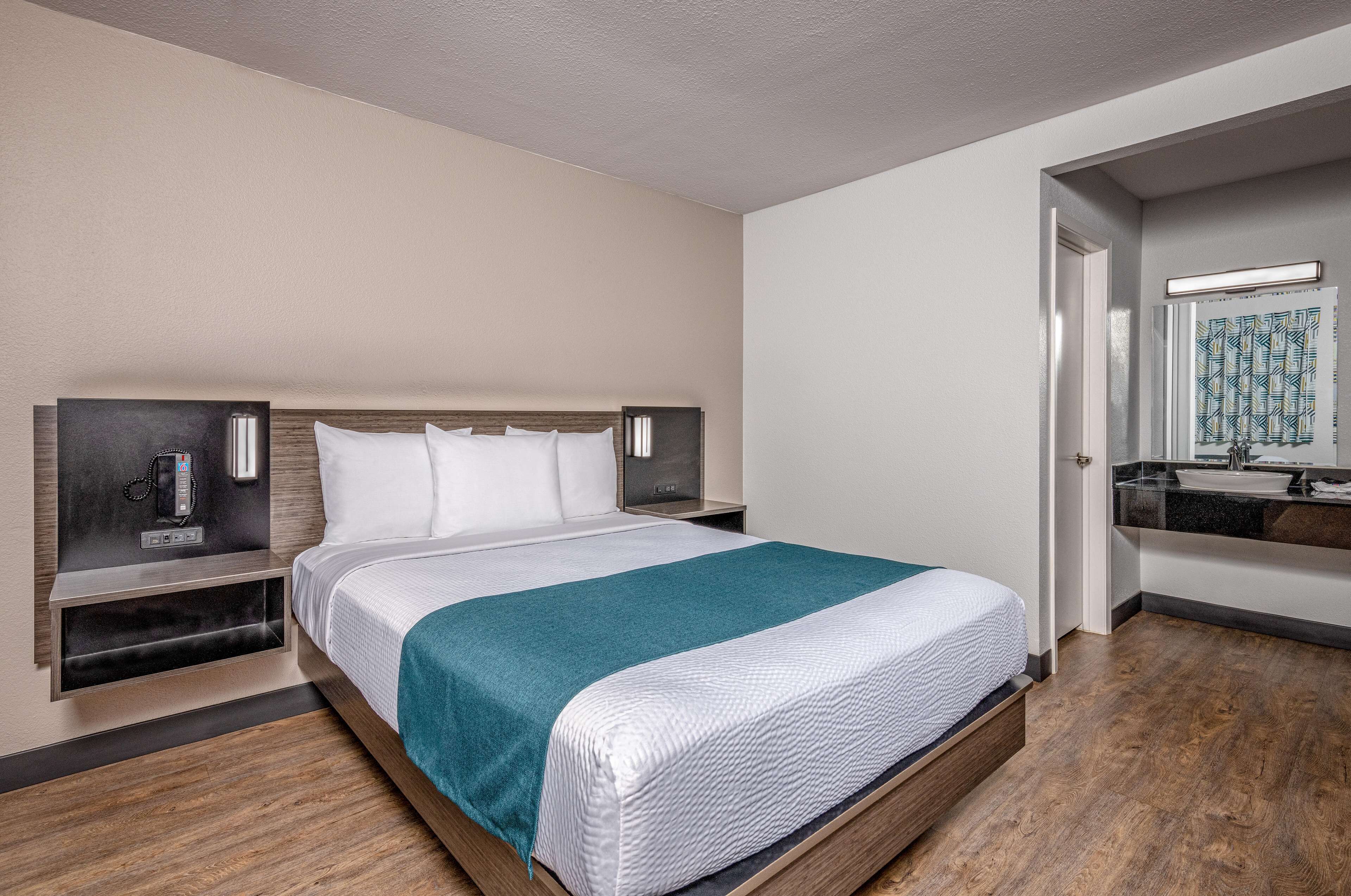 Una habitación de hotel con una cama grande, mesitas de noche, un espejo y un baño con lavamanos y espejo.