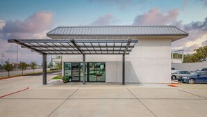 A modern building with a covered entrance, glass doors, and a parking lot. - Motel 6 Euless, TX - Dallas (Euless)