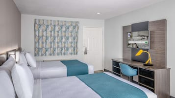 Habitación de hotel con dos camas, un escritorio con silla, un espejo grande y una cortina estampada.