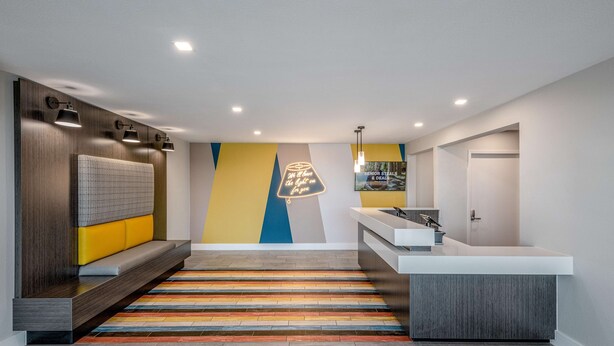 A modern hotel lobby with a reception desk, seating area, and a colorful striped rug. - Motel 6 Euless, TX - Dallas (Euless)