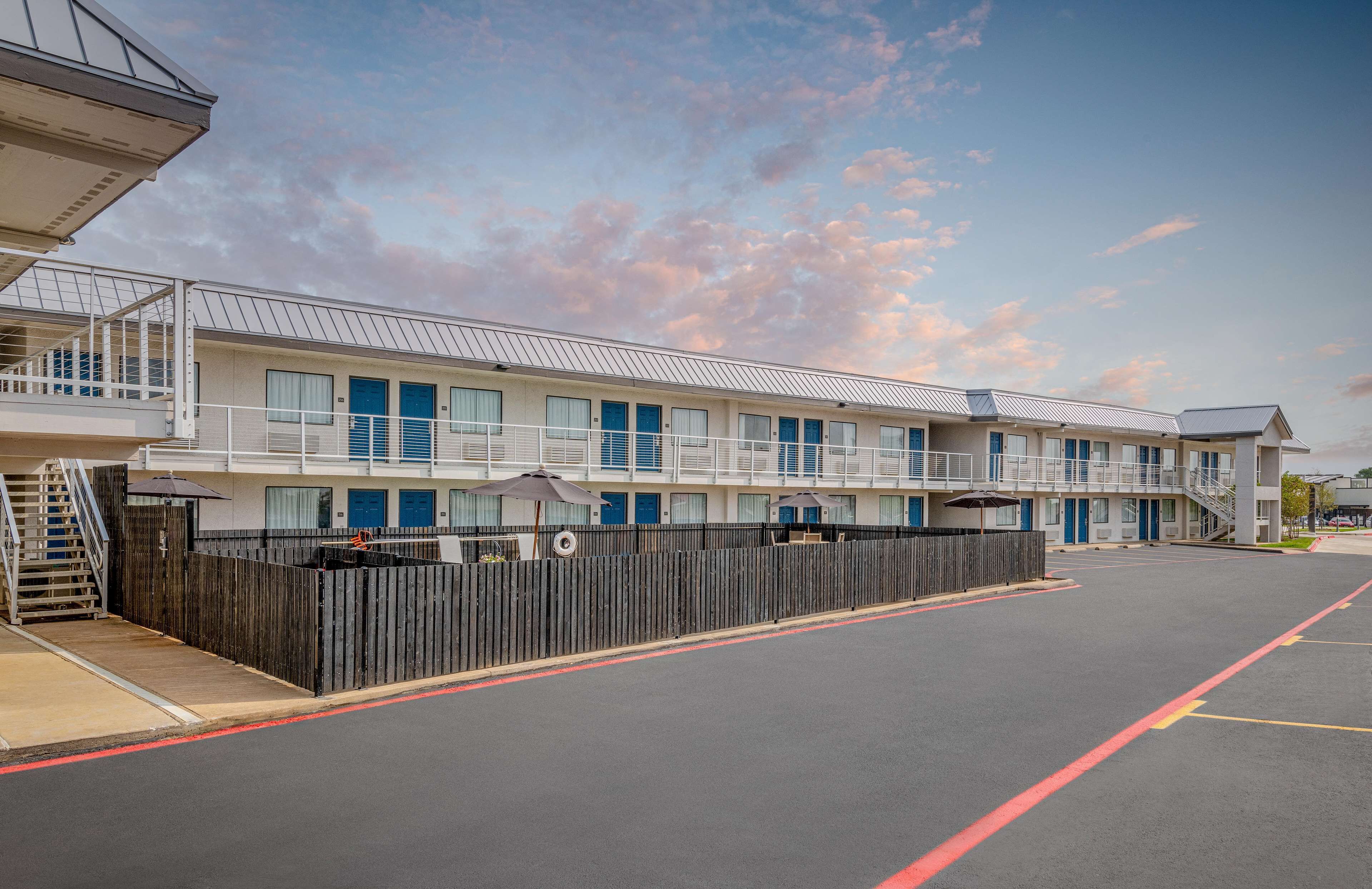 A motel with a row of rooms, a covered outdoor area, and a fenced parking lot.