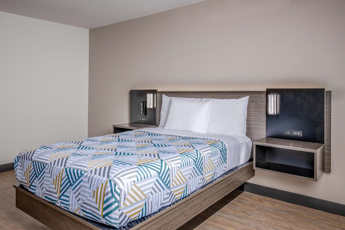 A modern hotel room with a bed, nightstands, and built-in shelves.