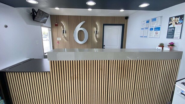 Una recepción con un diseño de listones de madera, un gran letrero con el número '6' y una puerta a la derecha.