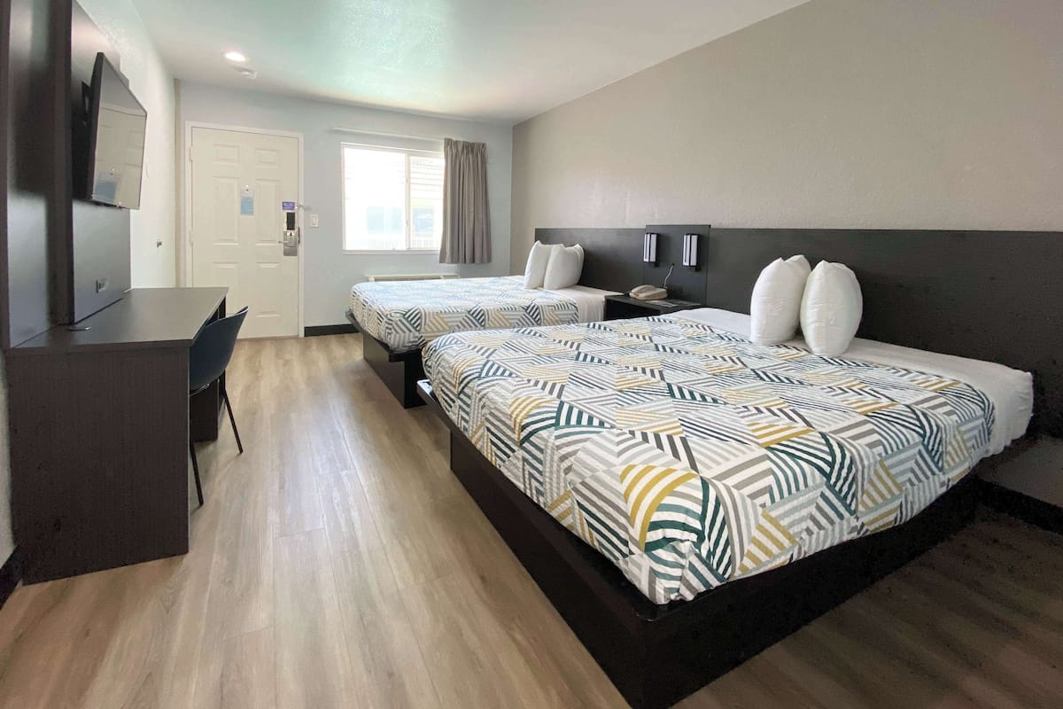 Quarto de hotel com duas camas, uma escrivaninha, uma cadeira, uma televisão e uma janela com cortinas.