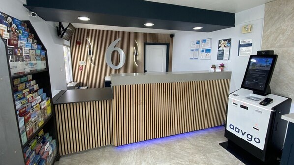 A reception desk with a wooden panel design, a digital kiosk, and a magazine rack. - Motel 6 Costa Mesa, CA (Costa Mesa)