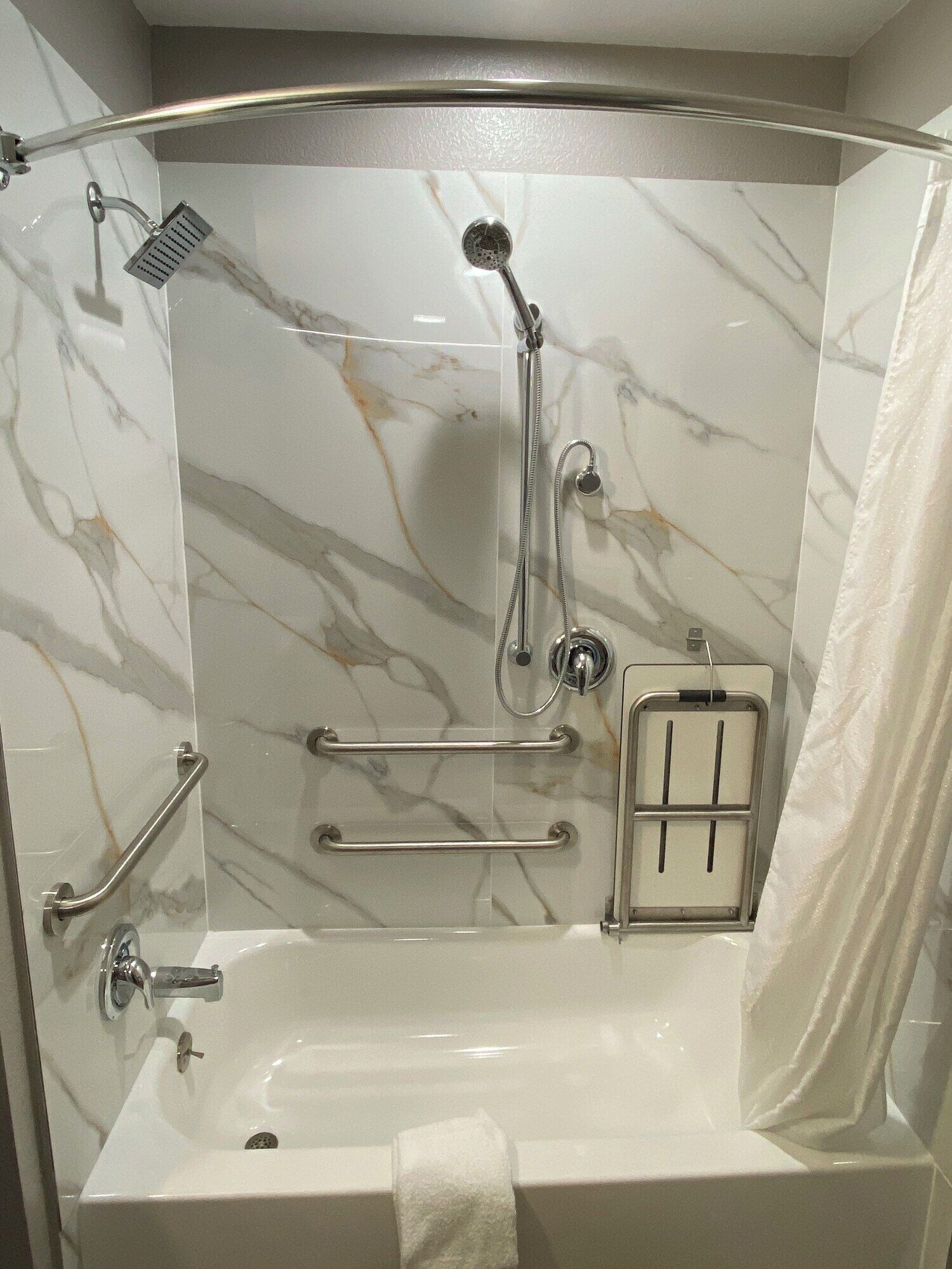 A walk-in shower with a glass door, marble walls, and a grab bar.