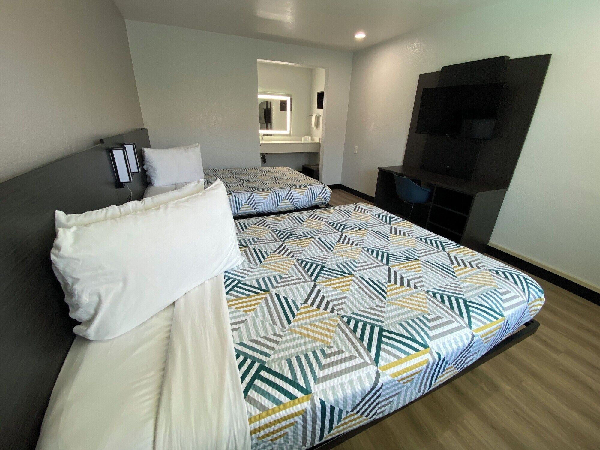 A hotel room with two beds, a TV, and a bathroom visible through an open door.