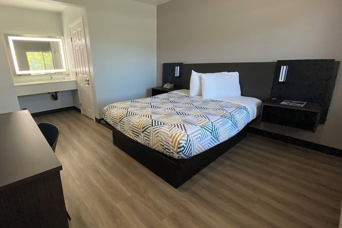 Quarto de hotel com cama, mesas de cabeceira, escrivaninha e janela com vista.