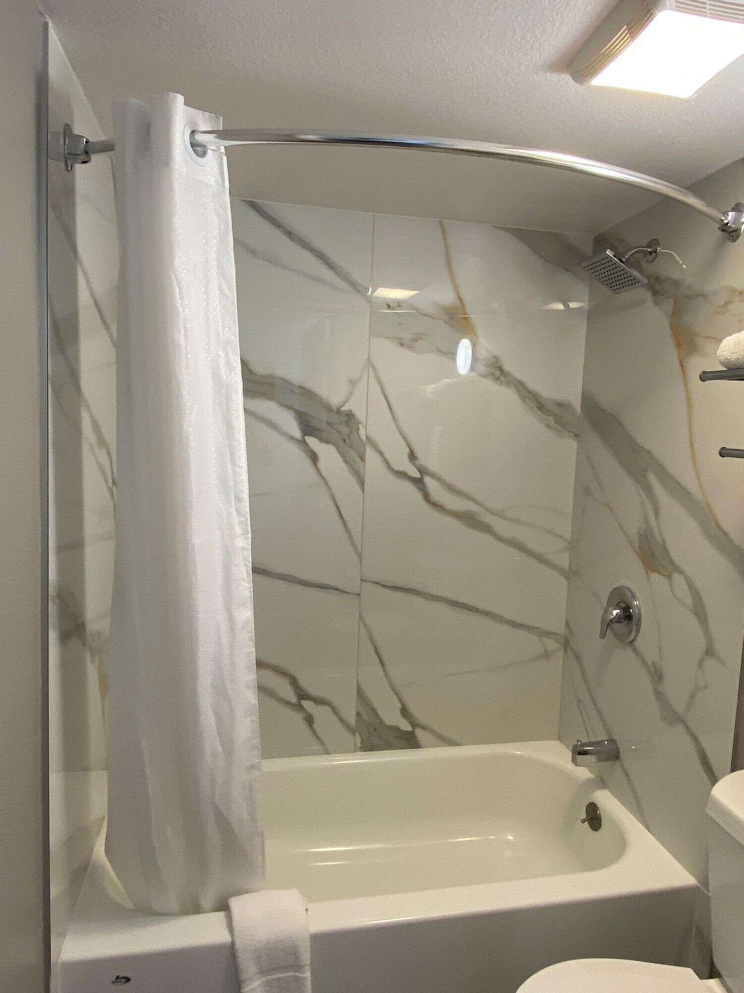 Un baño con pared de ducha de mármol, una bañera y un inodoro.