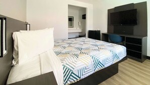 Habitación de hotel con cama, escritorio, silla, televisor y baño visible a través de una puerta abierta.